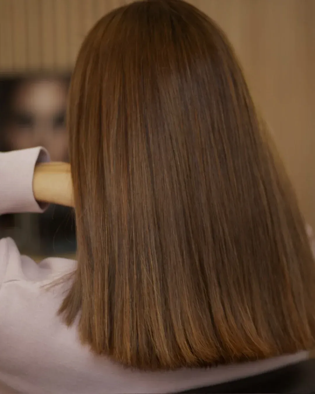 Mujer con cabello largo, liso y castaño, mirándose en un espejo.