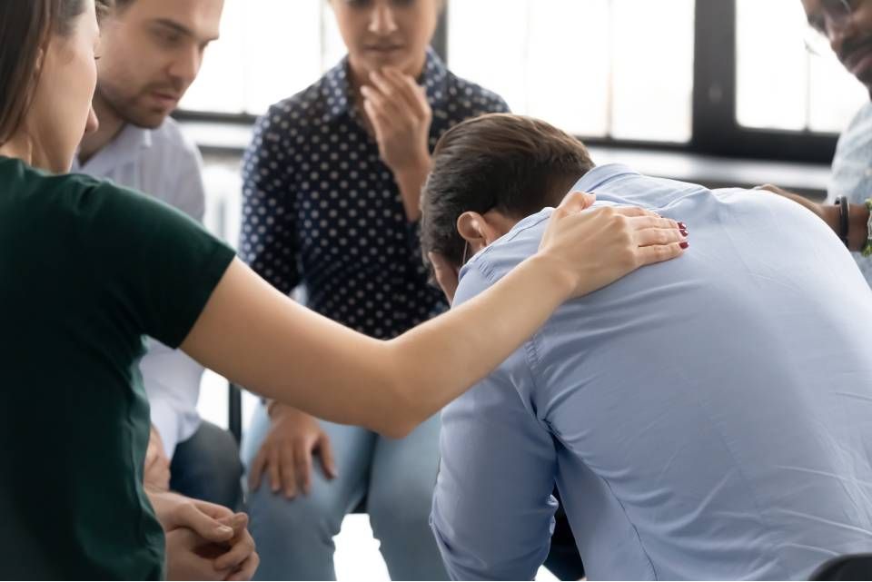 Collega's troosten een overstuurde collega in een lichte vergaderruimte op kantoor.