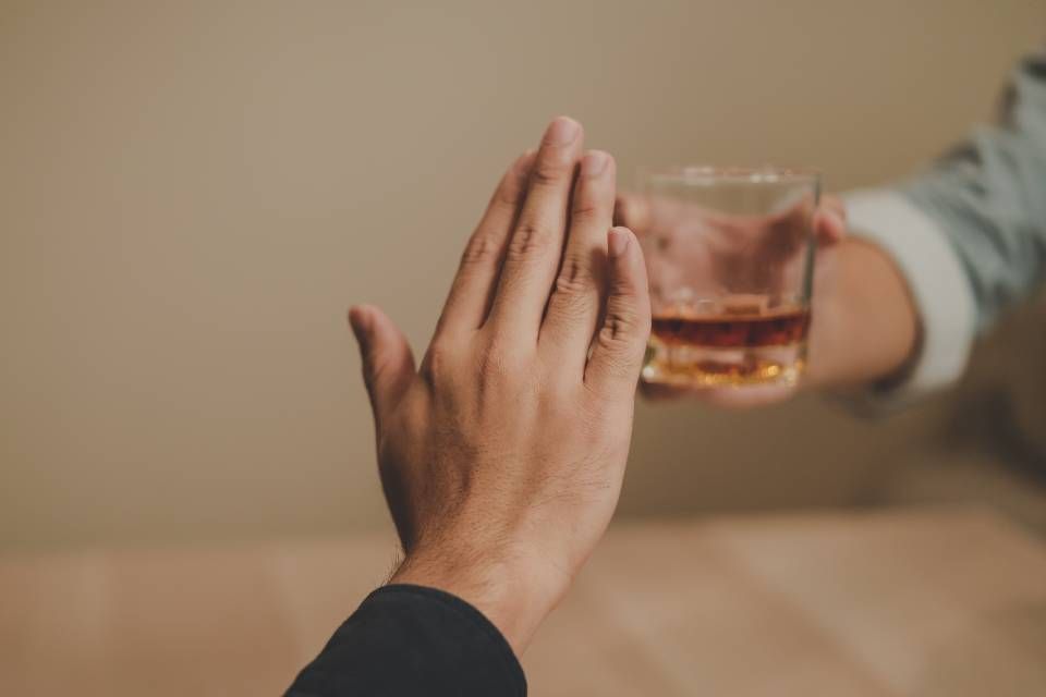 Twee handen klinken met glazen met amberkleurige drankjes aan een tafel.