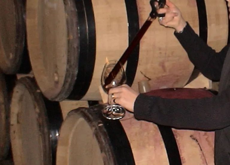 Persona vertiendo vino tinto desde un grifo de barril a un vaso en una bodega.
