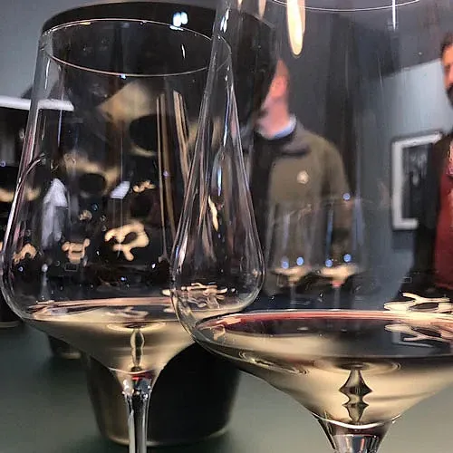 Dos copas de vino con líquido de color claro, que reflejan a una persona en un interior oscuro.