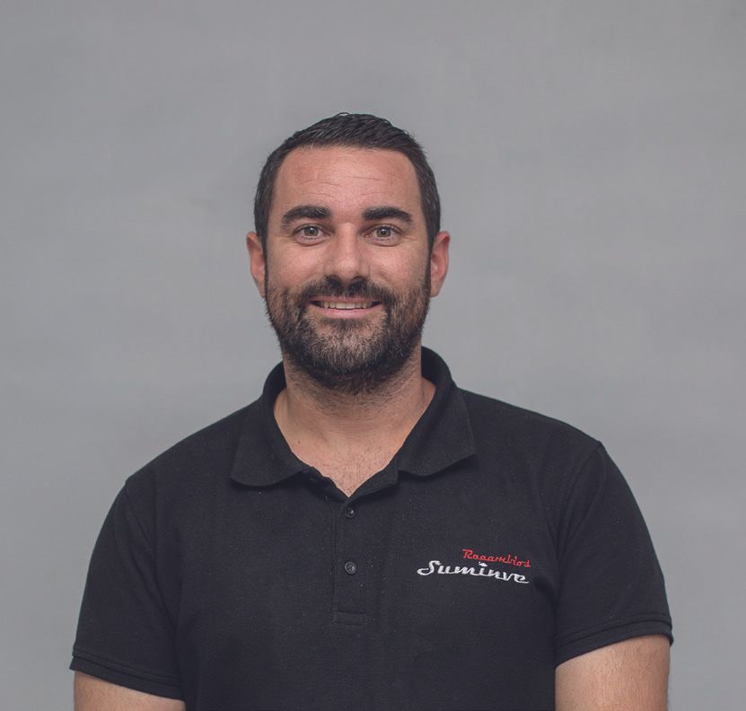 Un hombre con barba viste un polo negro y sonríe.