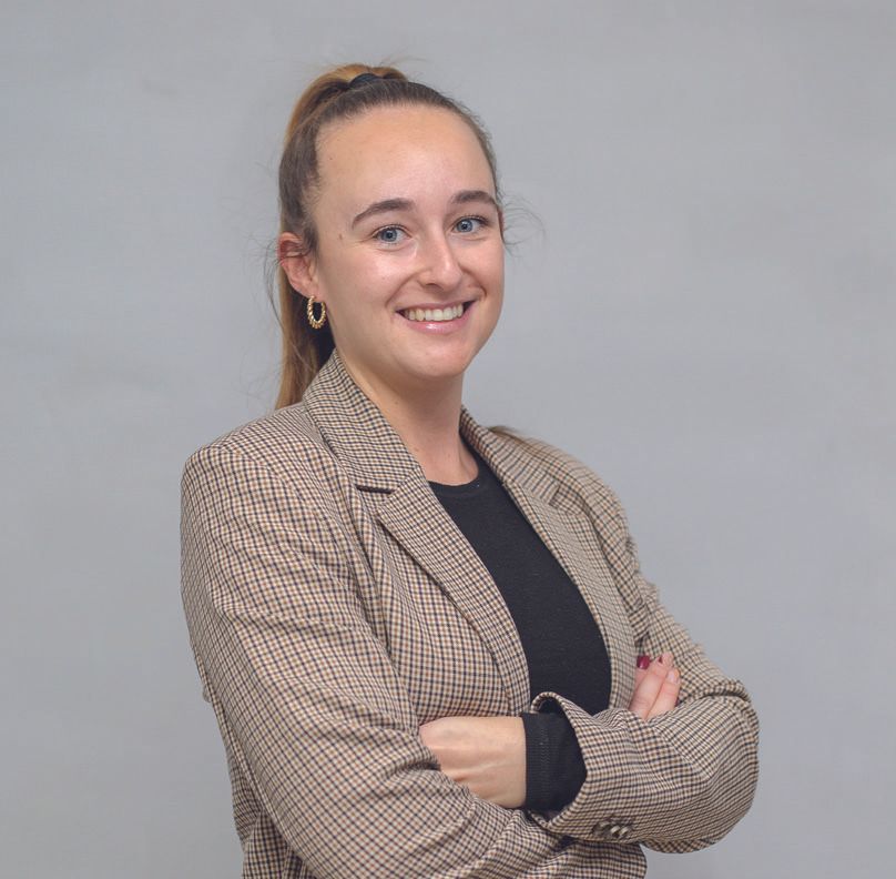 Una mujer con una chaqueta a cuadros sonríe con los brazos cruzados.