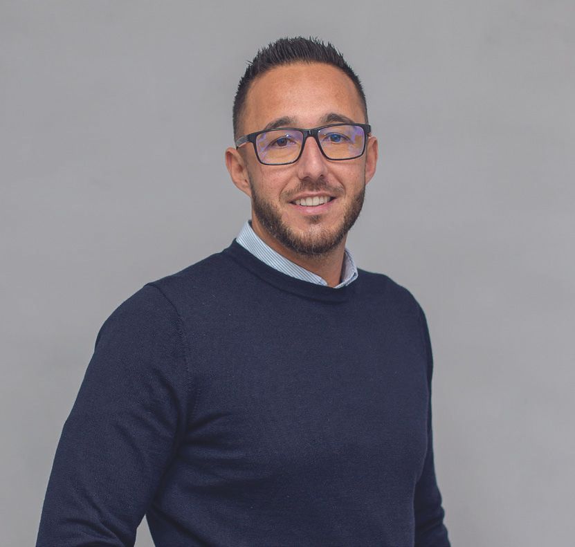 Un hombre que lleva gafas y un suéter azul sonríe para la cámara.