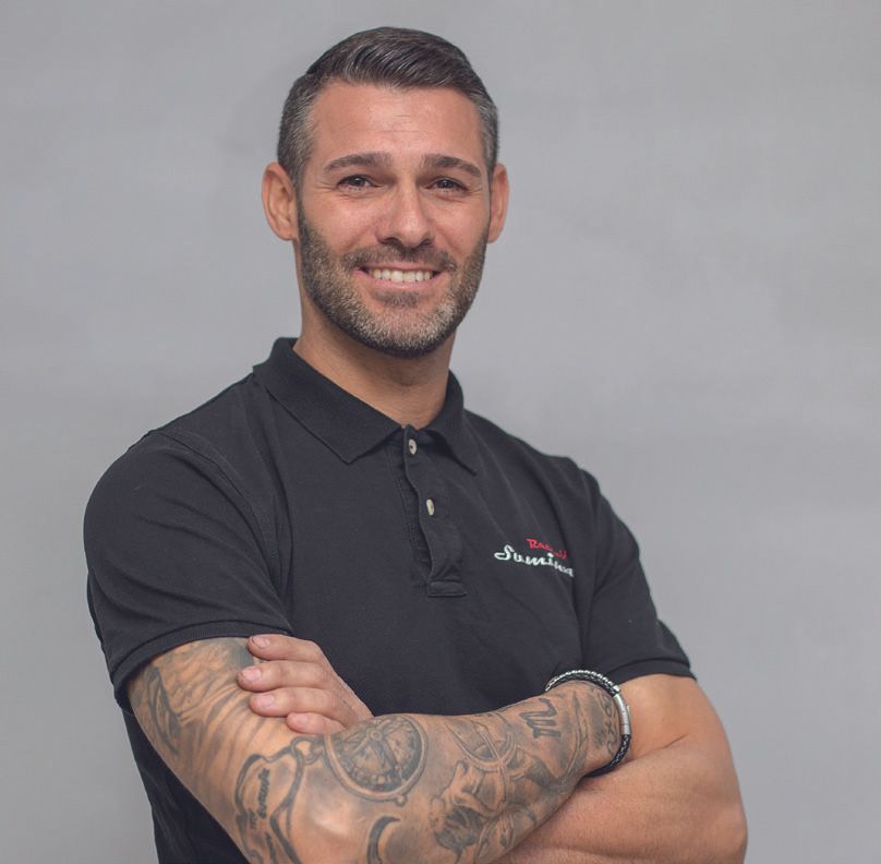 Un hombre con tatuajes en los brazos lleva un polo negro.