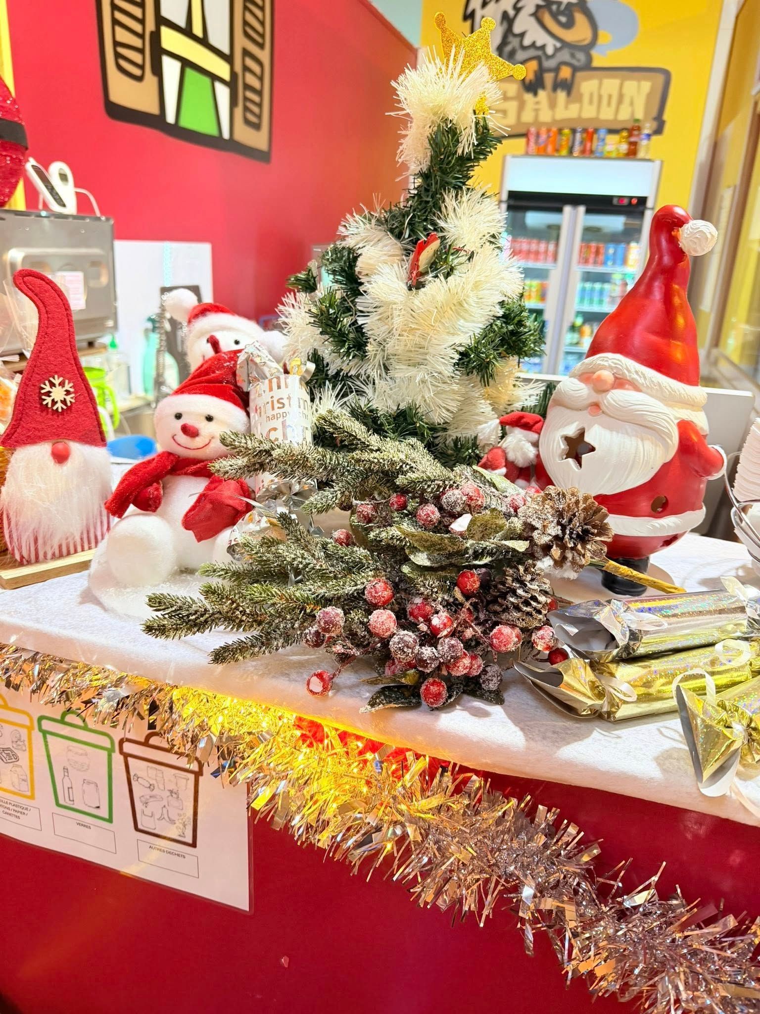Décorations de Noël sur fond rouge, comprenant un bonhomme de neige, une figurine de Père Noël et des petits sapins, avec des guirlandes dorées.