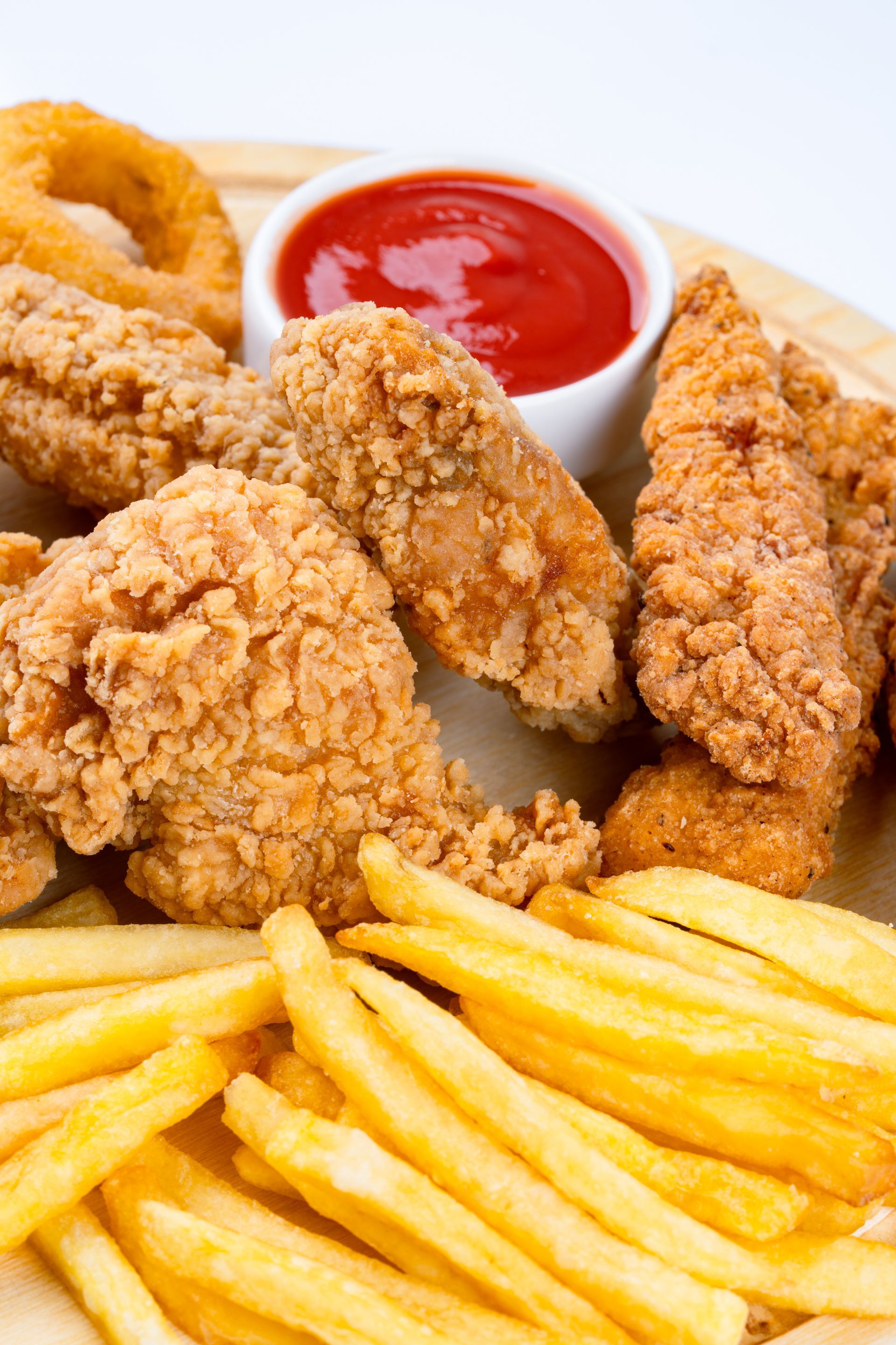 Aiguillettes de poulet panées, rondelles d'oignon et frites sur une assiette avec du ketchup.
