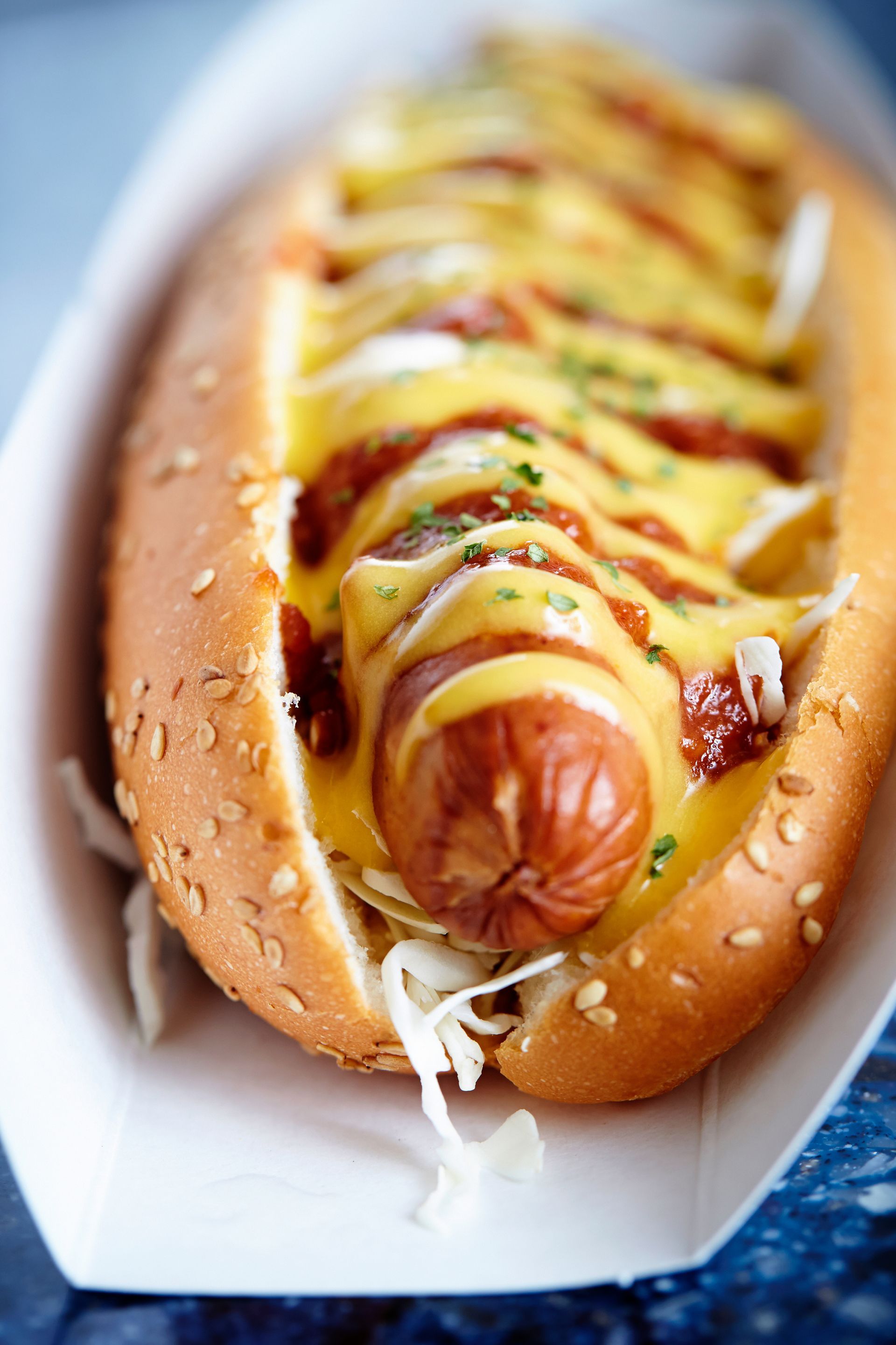 Hot-dog dans un pain aux graines de sésame, garni de moutarde, de ketchup et de chou râpé, dans un plateau en papier.