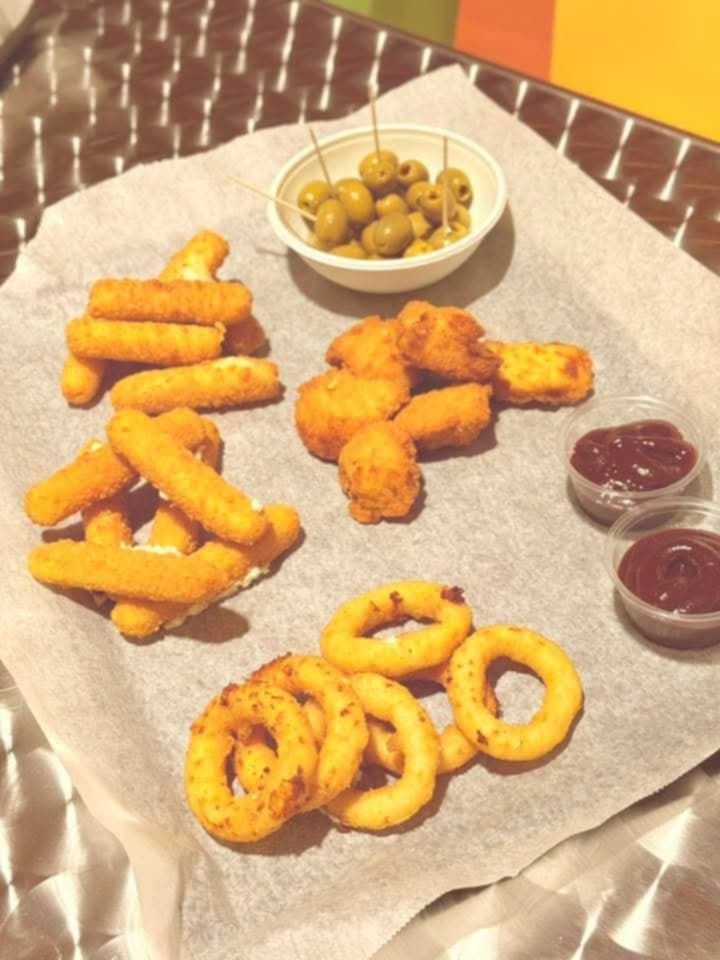Assiette d'amuse-gueules avec bâtonnets de mozzarella frits, nuggets de poulet, rondelles d'oignon, olives et deux pots de ketchup.