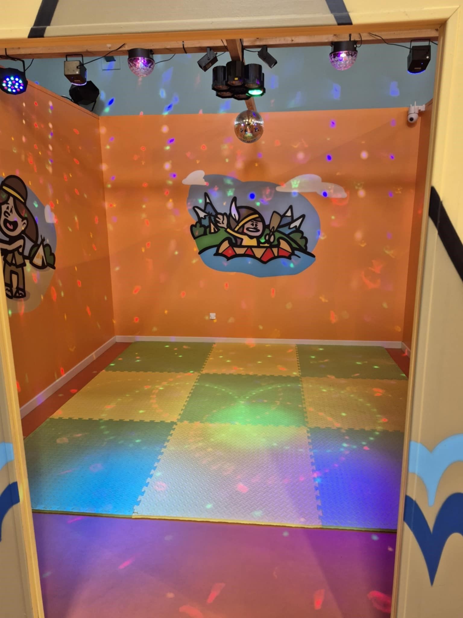 Petite salle de danse colorée avec lumières disco, boule à facettes et tapis de sol.