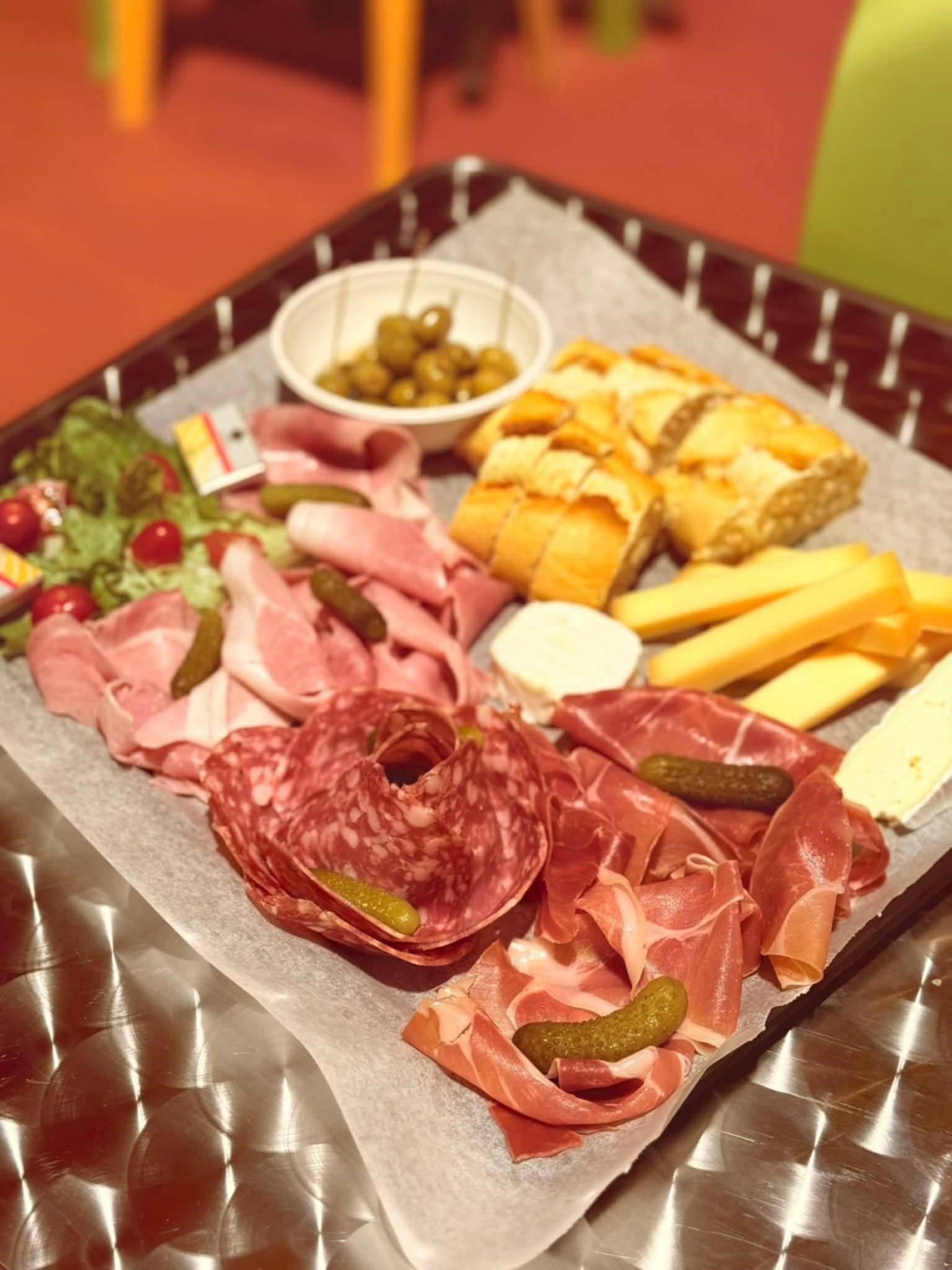 Planche de charcuterie avec viandes, fromages, pain, olives et cornichons sur un plateau carré.