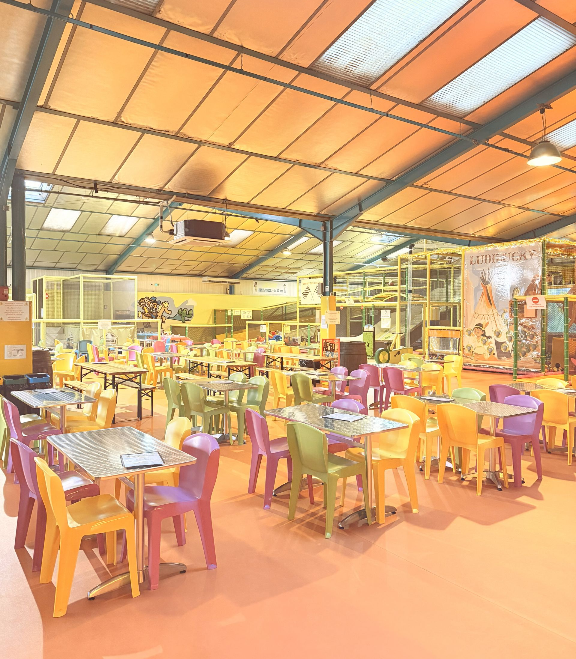 Aire de jeux intérieure avec tables et chaises colorées sous un haut plafond.