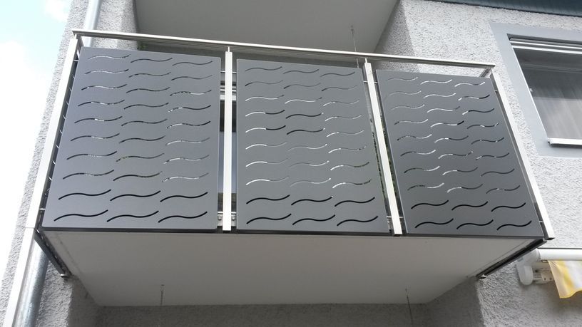 Graues Balkongeländer mit gewellten Ausschnitten und silbernem Rahmen.