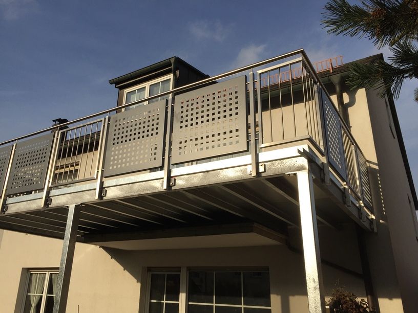Balkon mit Metallgeländer, ein helles Gebäude und ein klarer, sonniger Himmel.