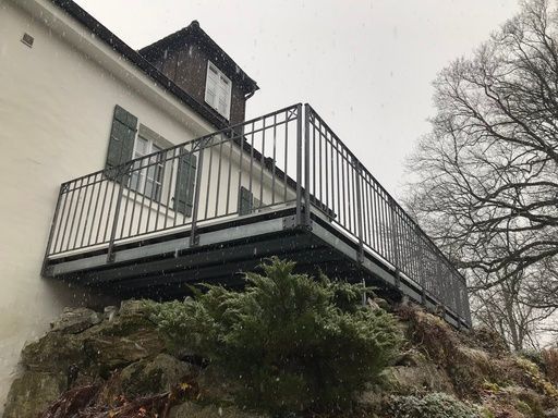 Balkon mit grauem Metallgeländer an einem weißen Haus, möglicherweise im Winter.