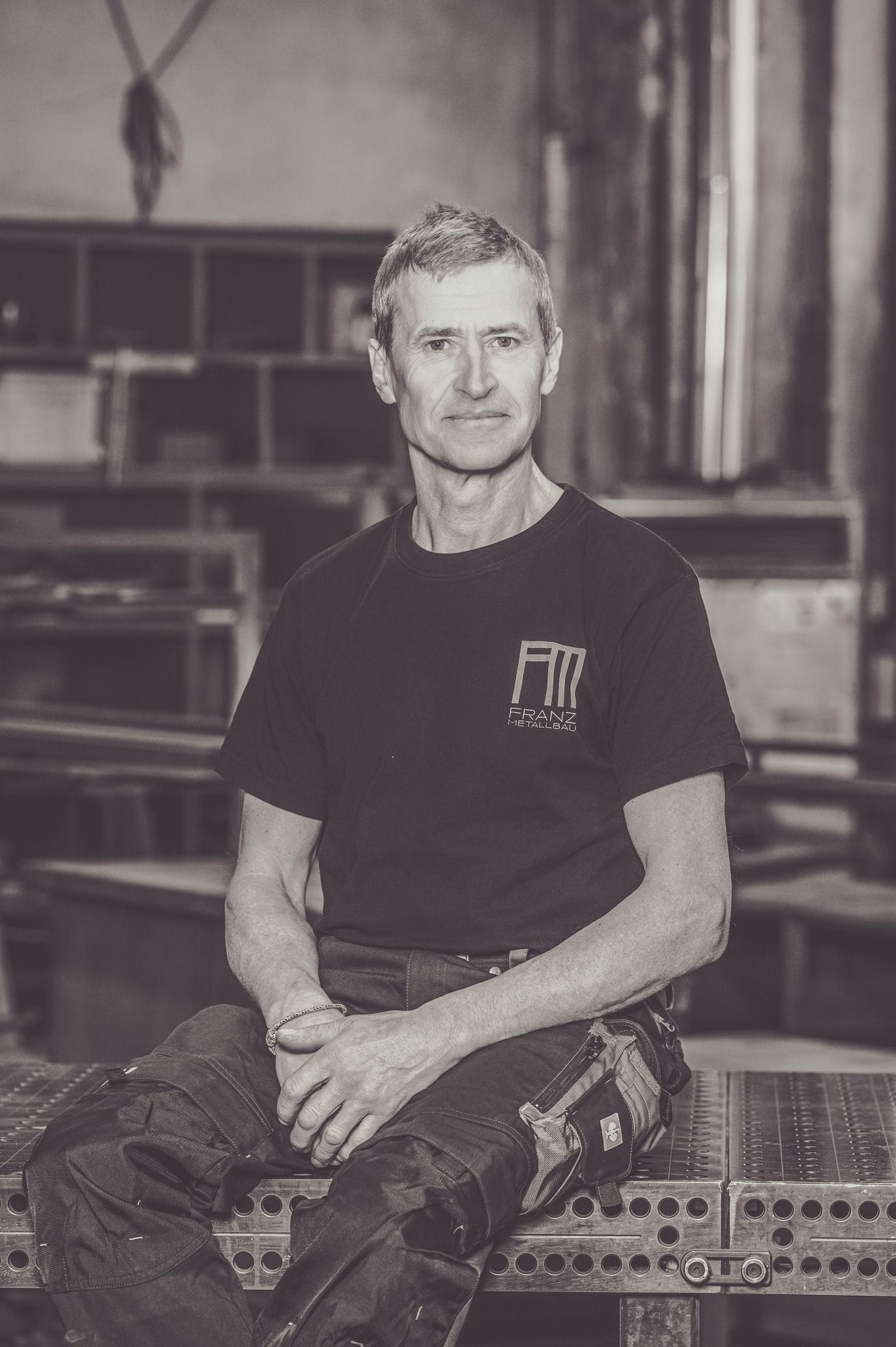 Mann in Arbeitskleidung sitzt in einer Werkstatt; Schwarzweißfoto.