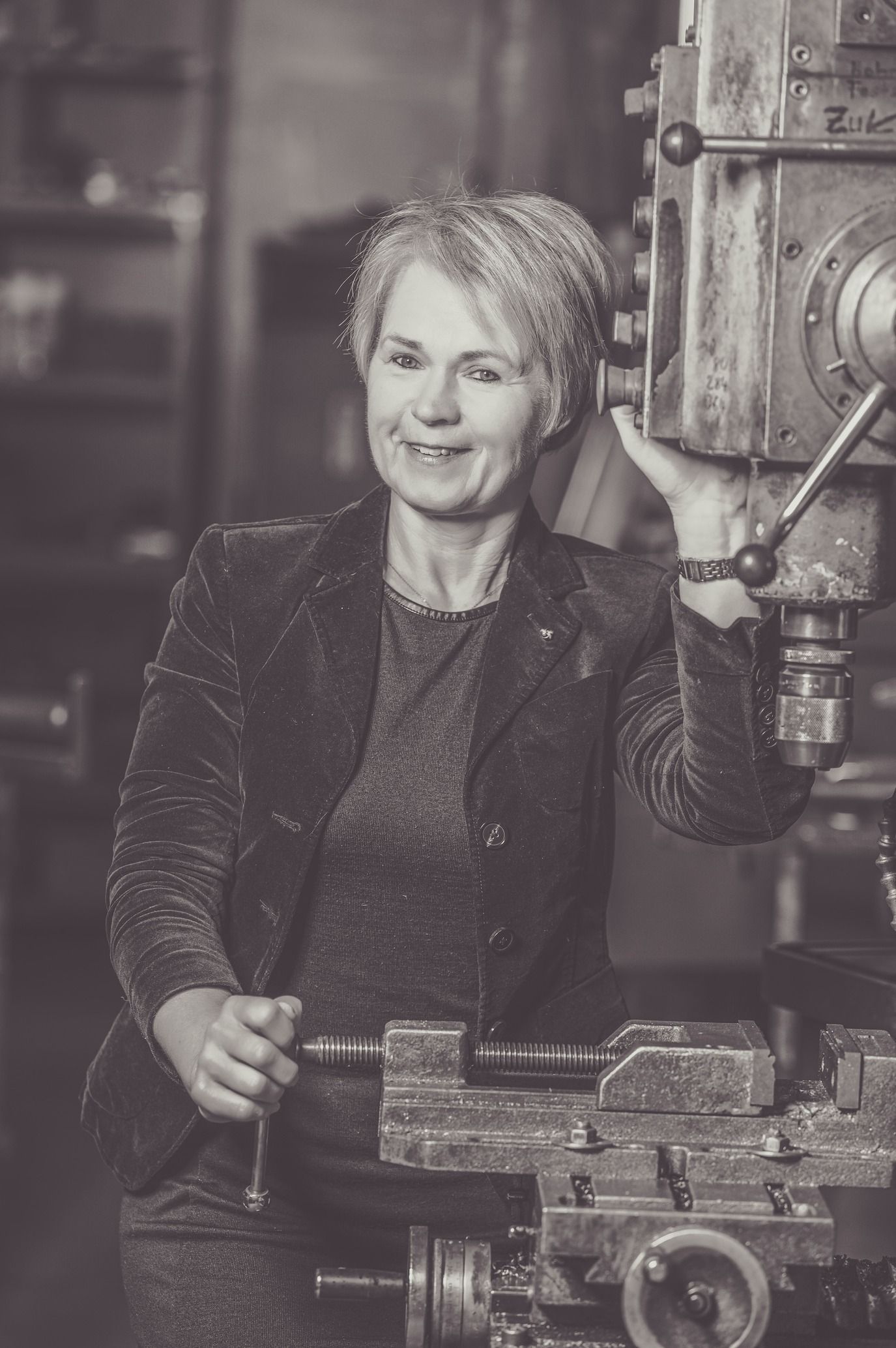 Frau bedient Maschinen in einer Werkstatt und lächelt in die Kamera. Schwarzweiß.