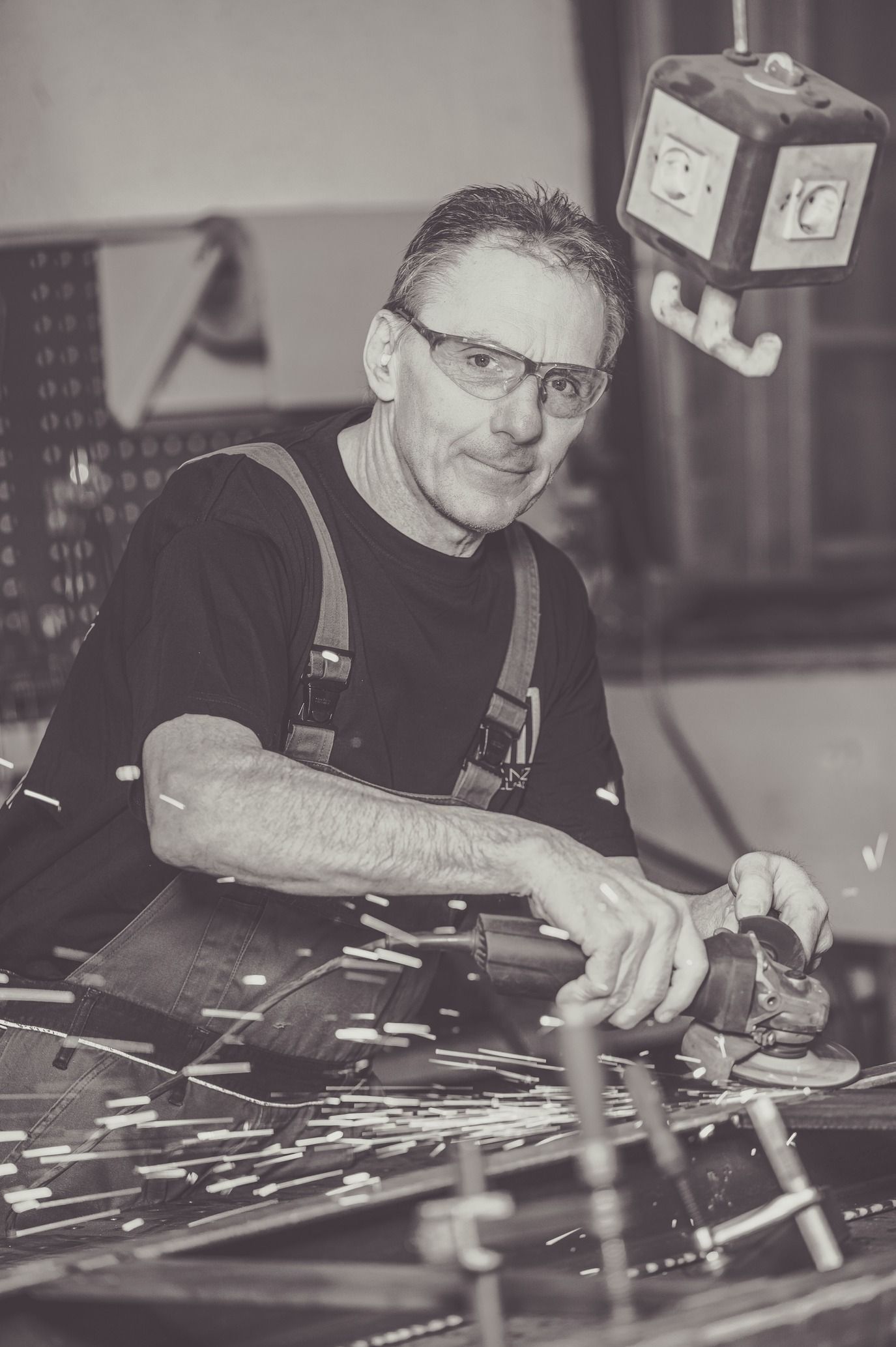 Mann benutzt eine Schleifmaschine, Funken fliegen. Er trägt eine Schutzbrille, eine Werkstattumgebung.