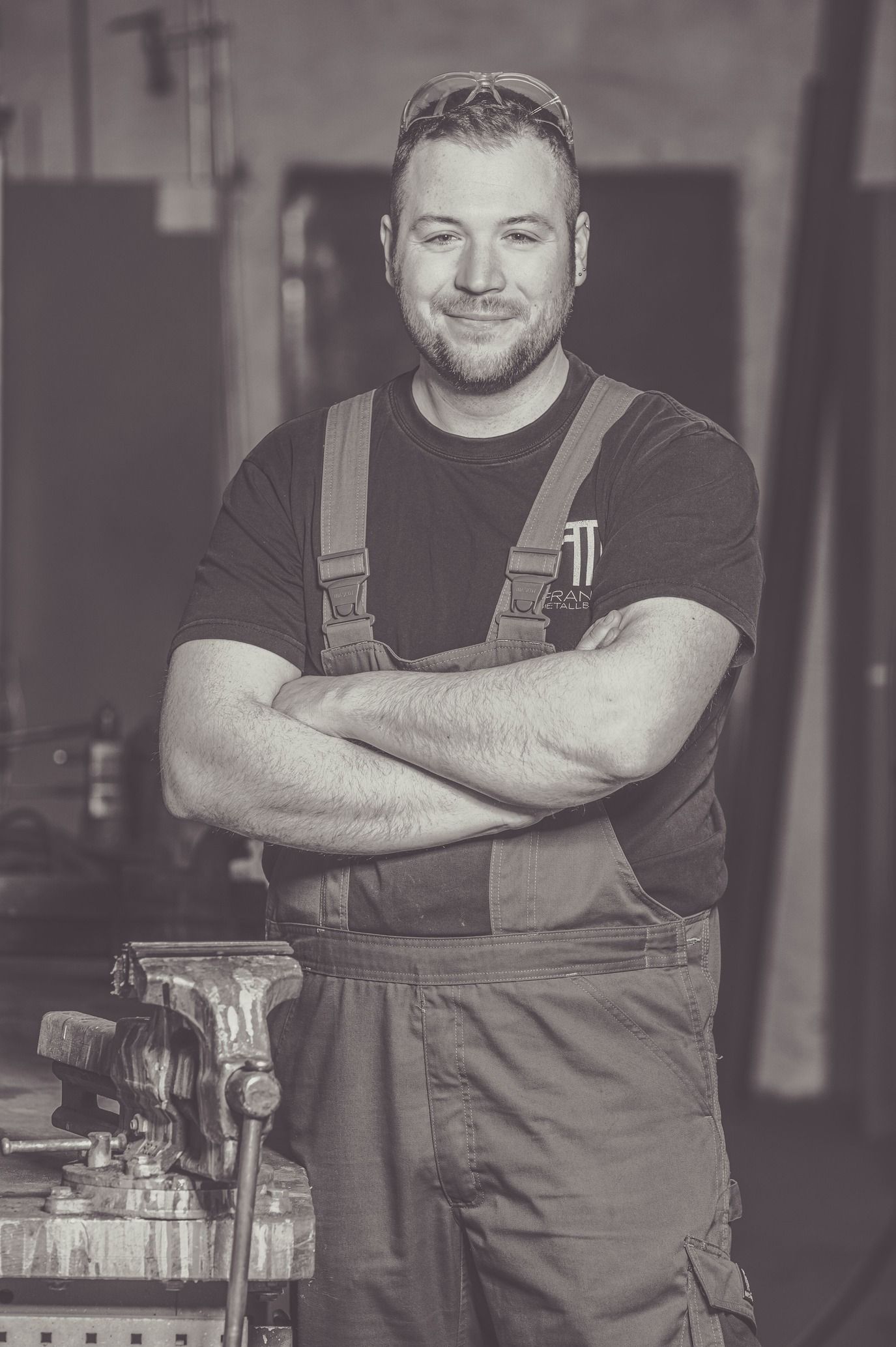 Mann in der Werkstatt, Arme verschränkt, lächelnd, mit Mütze und Arbeitskleidung.