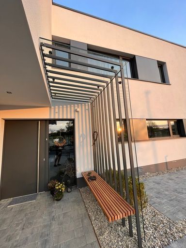 Moderner Hauseingang mit dunkelgrauer Tür, Holzbank und Metalldach.