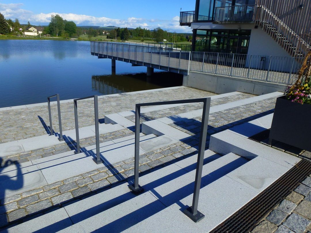 Stufen führen zu einem See mit einem Gebäude und einem Pier im Hintergrund, Handläufe für den Zugang.