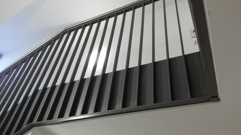 Graues Treppengeländer aus Metall vor weißen und grauen Wänden.