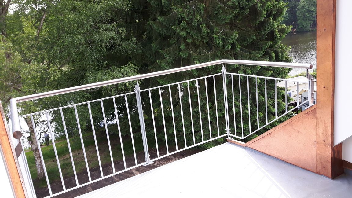 Edelstahlgeländer auf einem Balkon mit Blick ins Grüne und aufs Wasser.