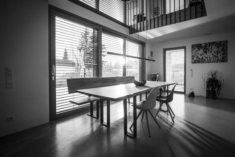 Modernes Esszimmer mit großen Fenstern, einem langen Tisch und minimalistischer Einrichtung.