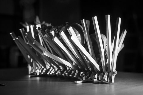 Abstrakte Metallskulptur mit vertikalen, Schatten werfenden Balken auf einem Tisch.