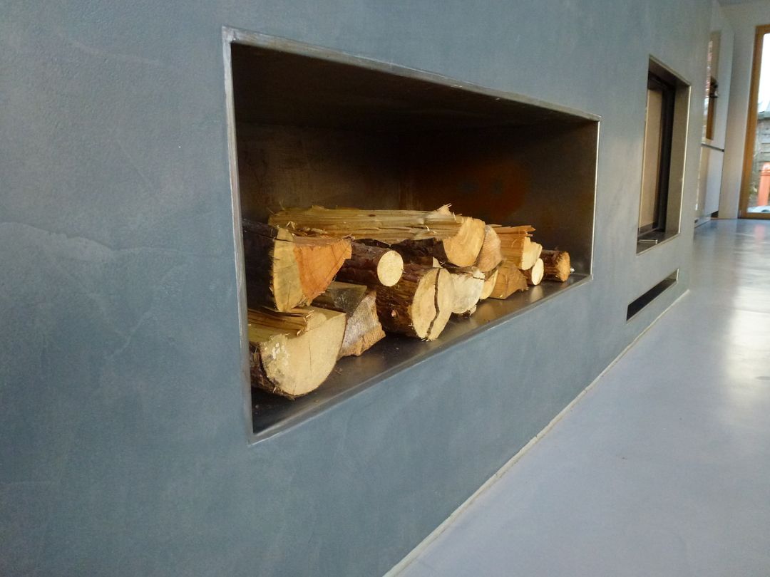 Brennholz ist in einer Nische in einer blaugrauen Wand neben einem Fenster gestapelt.