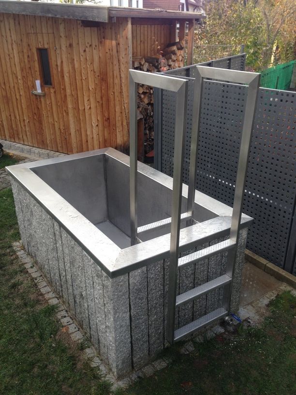 Stein-Whirlpool mit Metallrahmen und Leiter in einem Hof. Holzschuppen im Hintergrund.