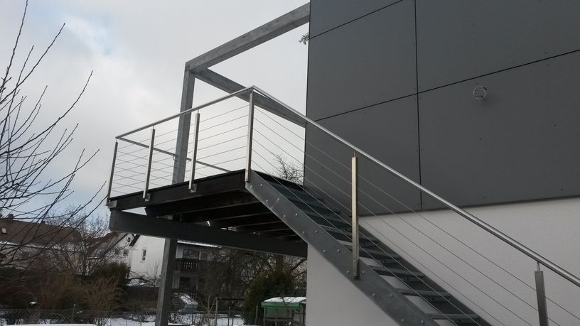 Metall-Außentreppe mit Kabelgeländer, befestigt an einem modernen grauen Gebäude. Schneebedeckter Boden.