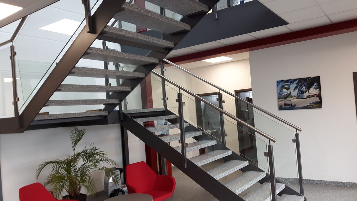 Treppe mit Metallrahmen und Glasgeländer, die in einem modernen Büroumfeld nach oben und hinüber führt.