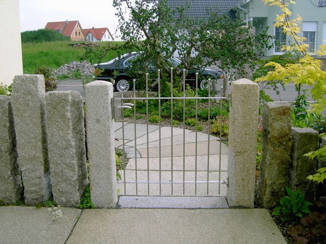 Ein Granittor in einem modernen Hof, umgeben von hohen Steinsäulen und einem gepflasterten Weg.