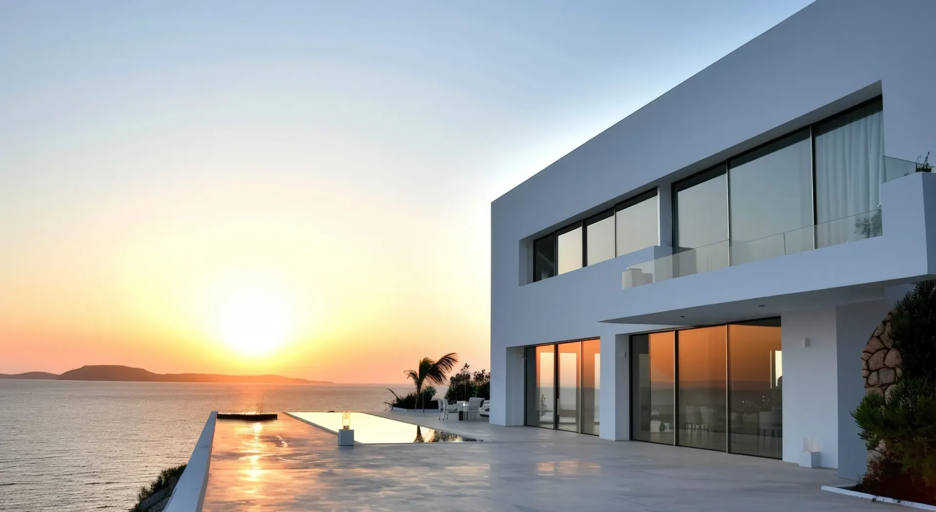 Una gran casa blanca con piscina con vistas al océano al atardecer.