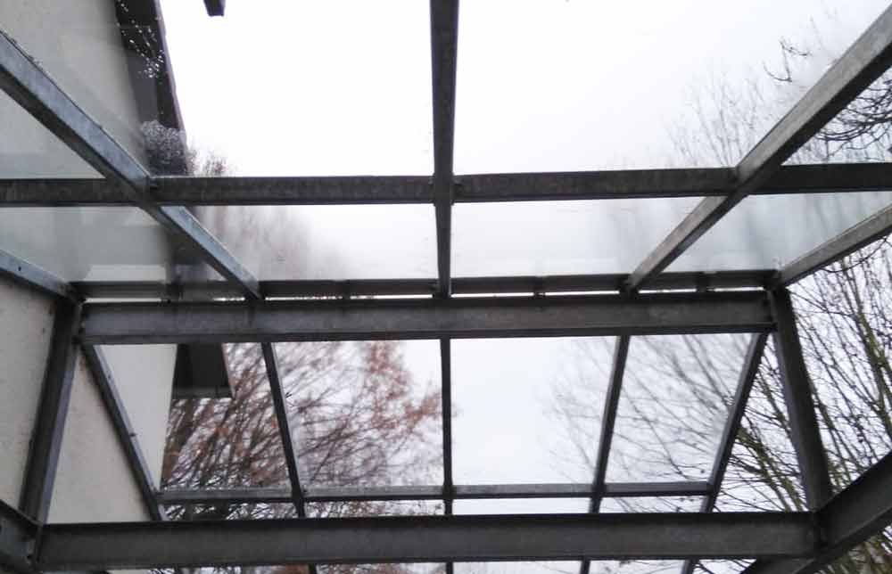 Blick nach oben auf ein Glasdach mit Bäumen im Hintergrund
