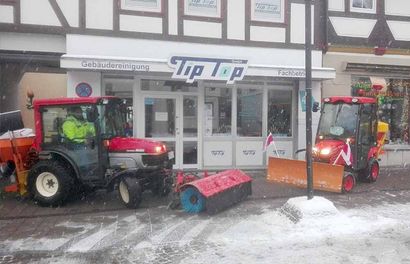 Vor einem Laden namens Tip Top parken zwei Traktoren.