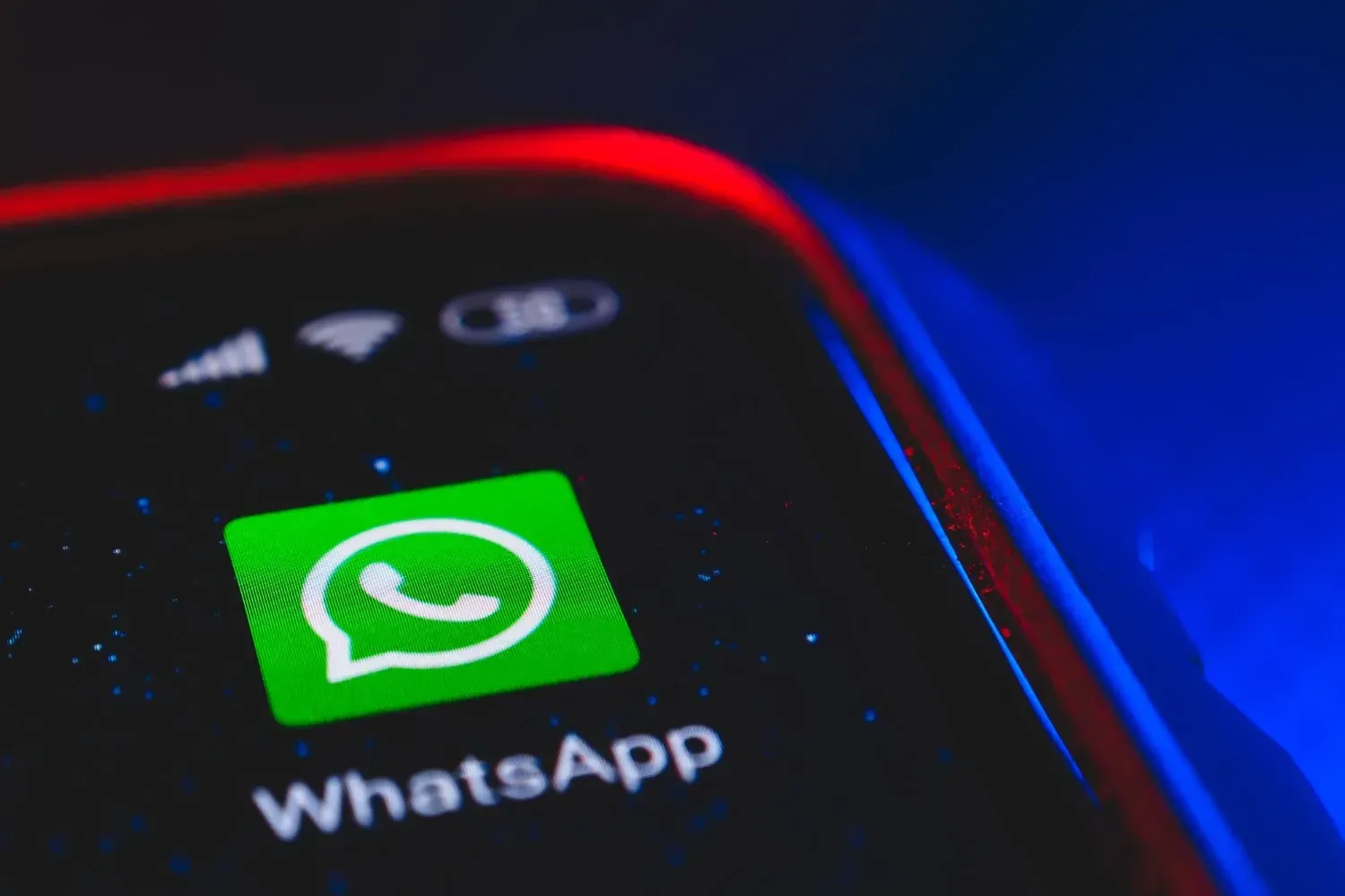 Pantalla de smartphone que muestra el icono de WhatsApp sobre un fondo oscuro, iluminado por un brillo azul.