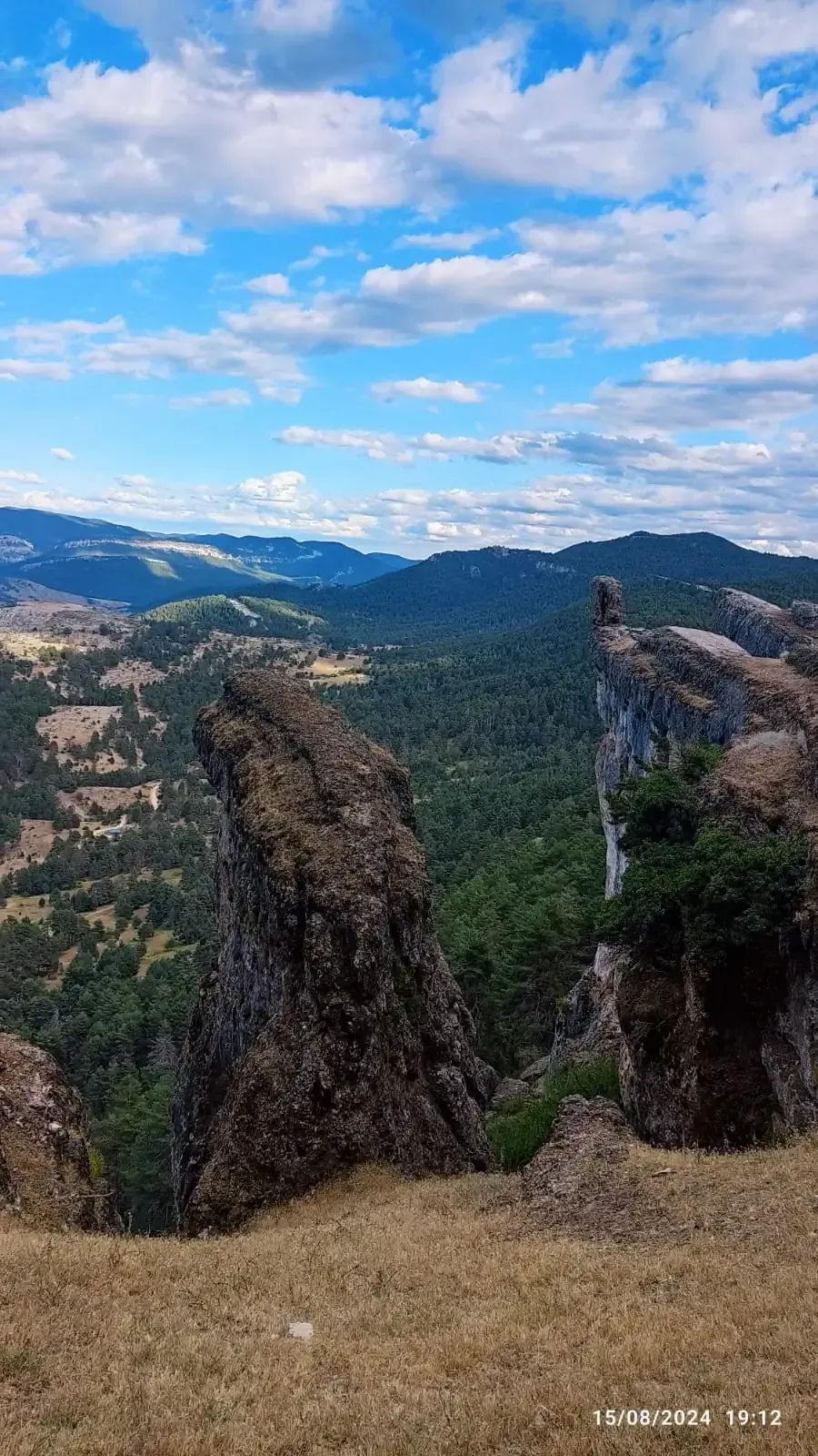 Una vista de una cadena montañosa con rocas en primer plano y árboles en el fondo.