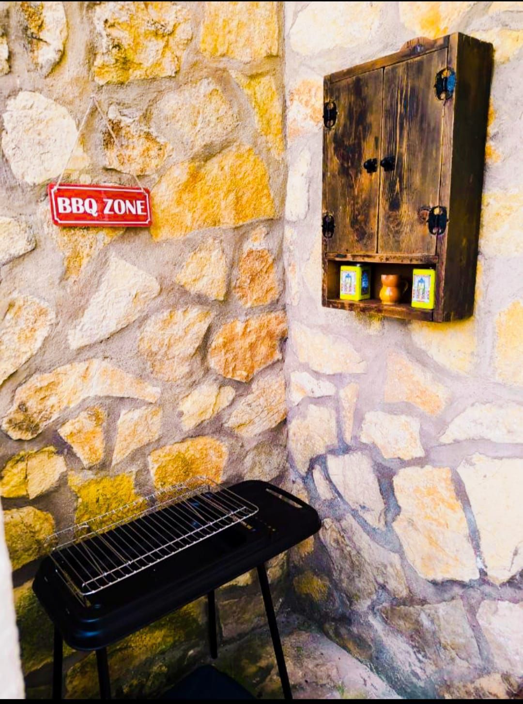 Un cartel de zona de barbacoa cuelga en una pared de piedra al lado de una parrilla.