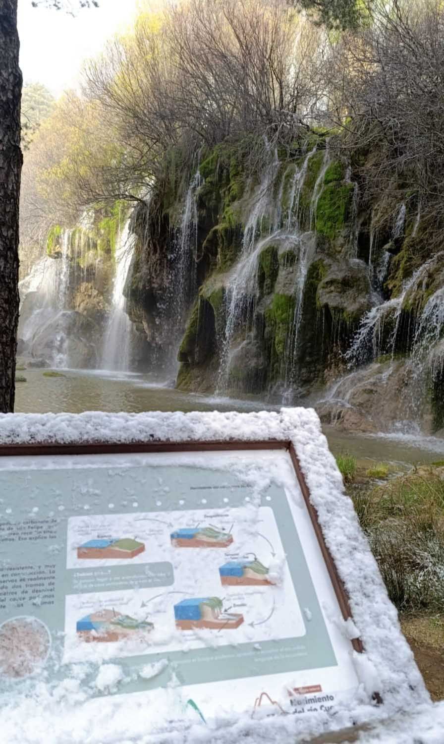 Un cartel está cubierto de nieve frente a una cascada.