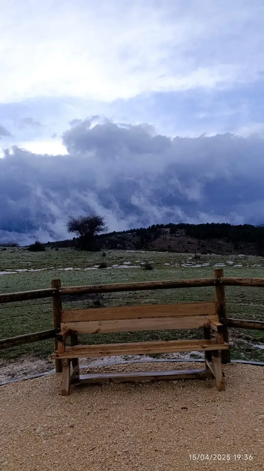 Un banco de madera está sentado en el medio de un campo con un cielo nublado en el fondo.