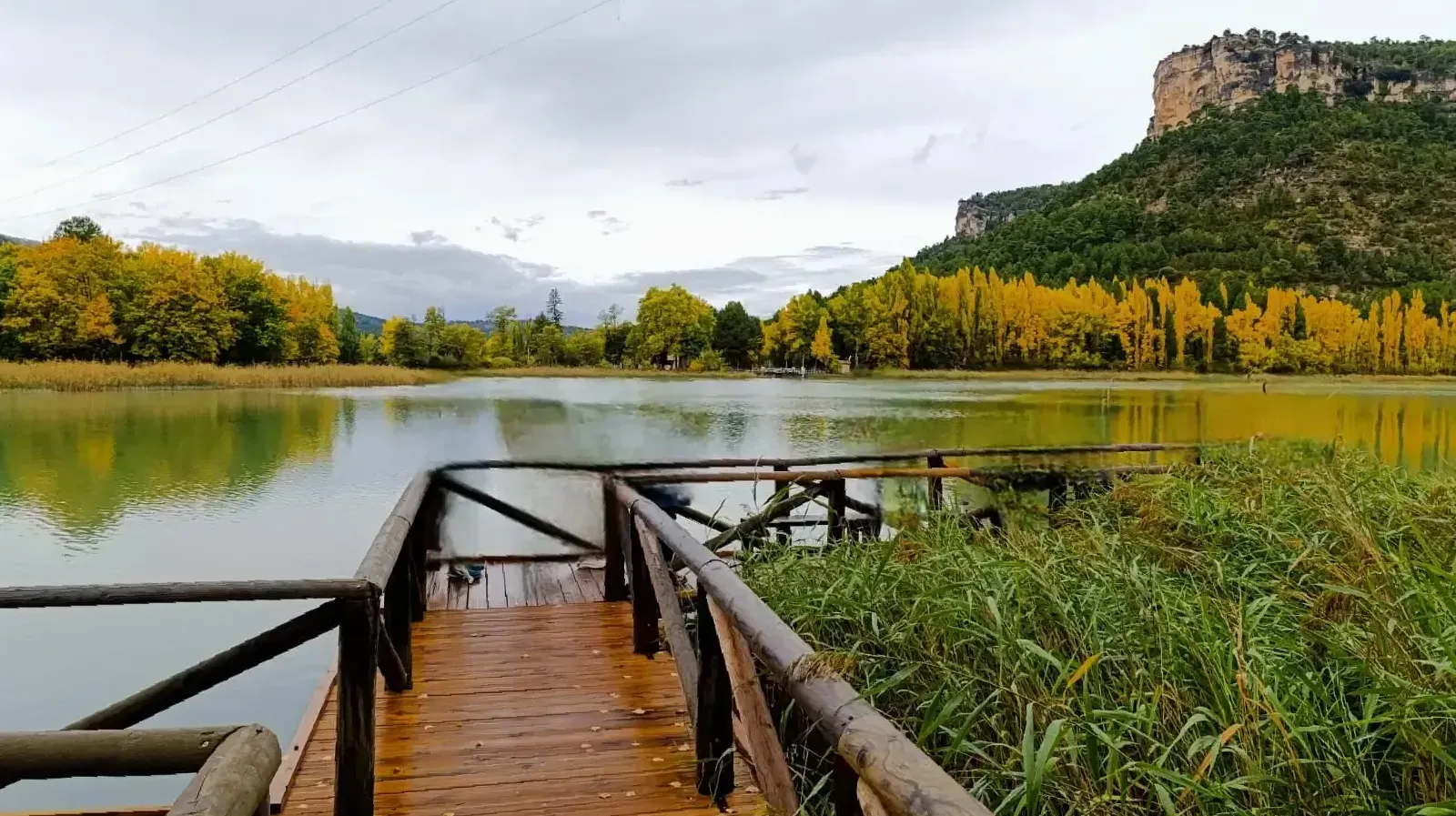 Un muelle de madera que conduce a un lago con una montaña al fondo.
