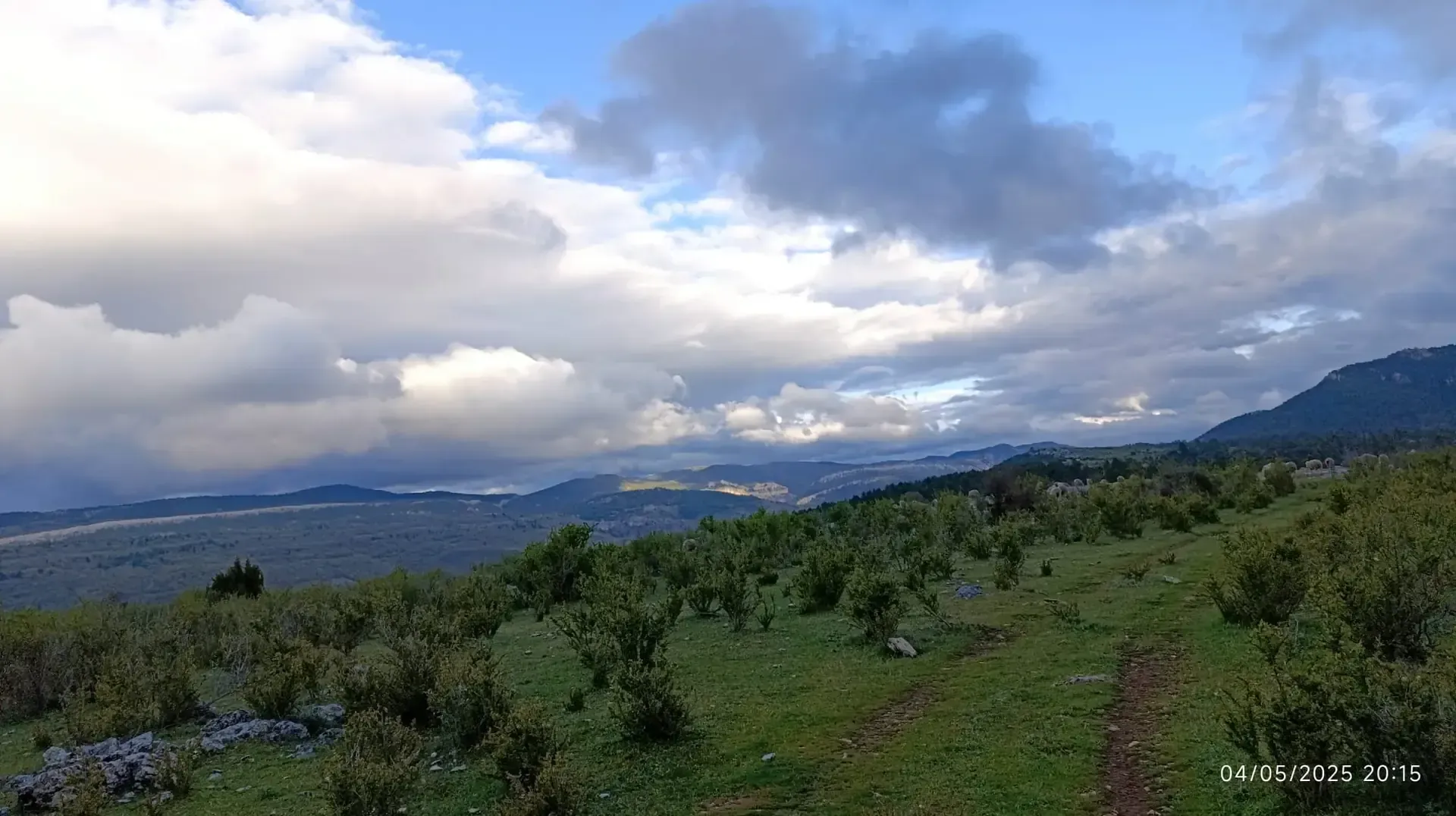Una vista de un campo con montañas al fondo y nubes en el cielo.