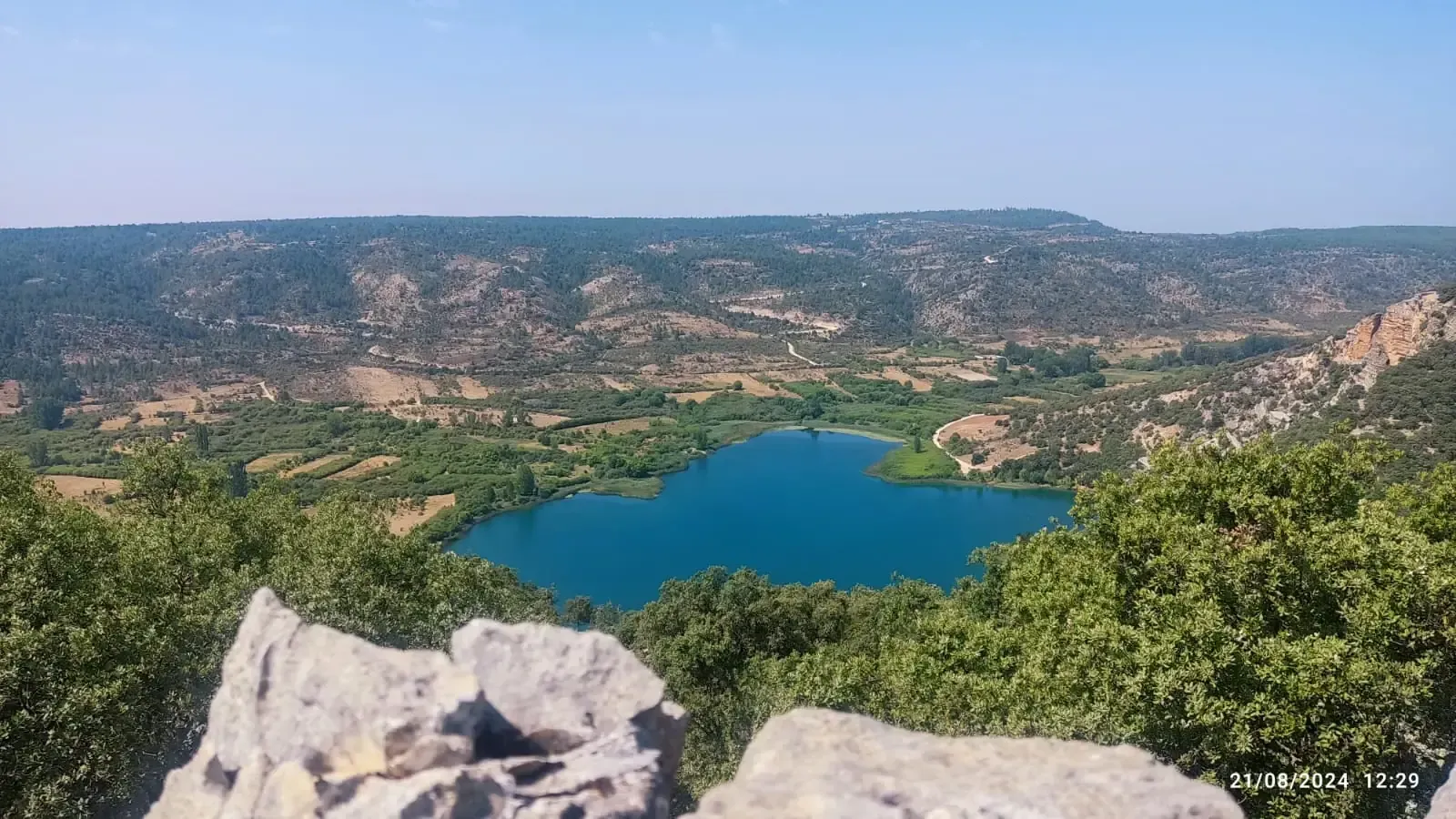 Una vista de un lago rodeado de árboles y rocas desde un acantilado.