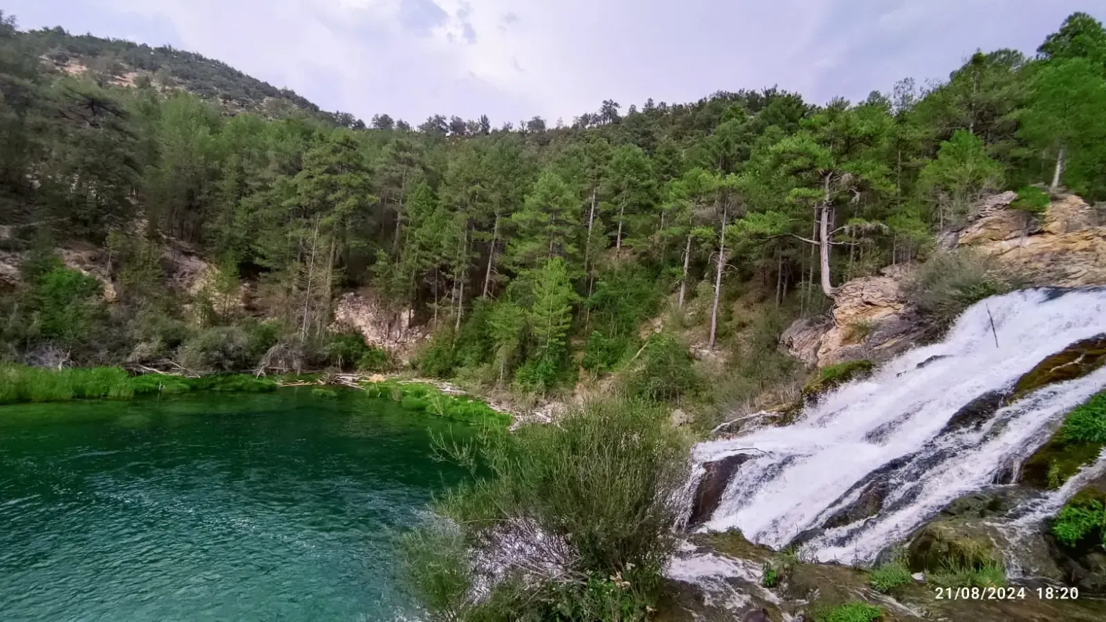 Una cascada en medio de un bosque al lado de un lago.