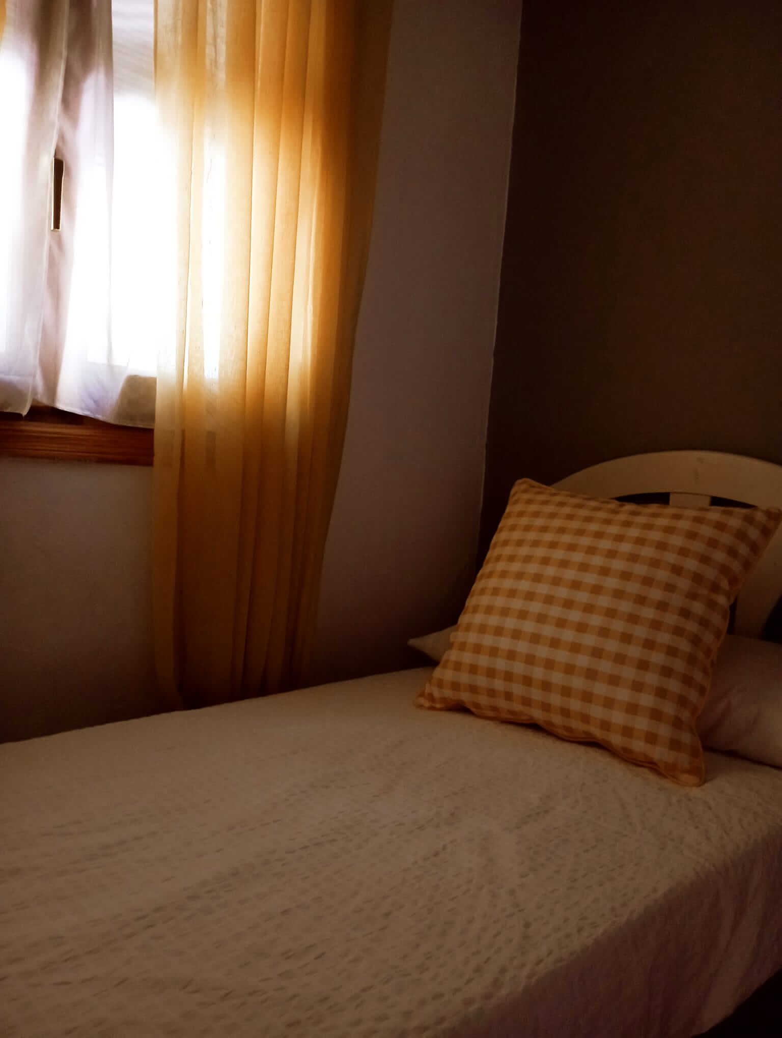 Una cama con una almohada a cuadros frente a una ventana.