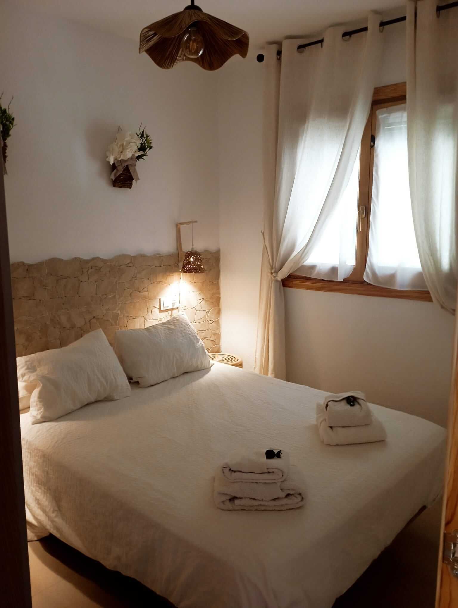 Un dormitorio con una cama y una ventana con cortinas blancas.