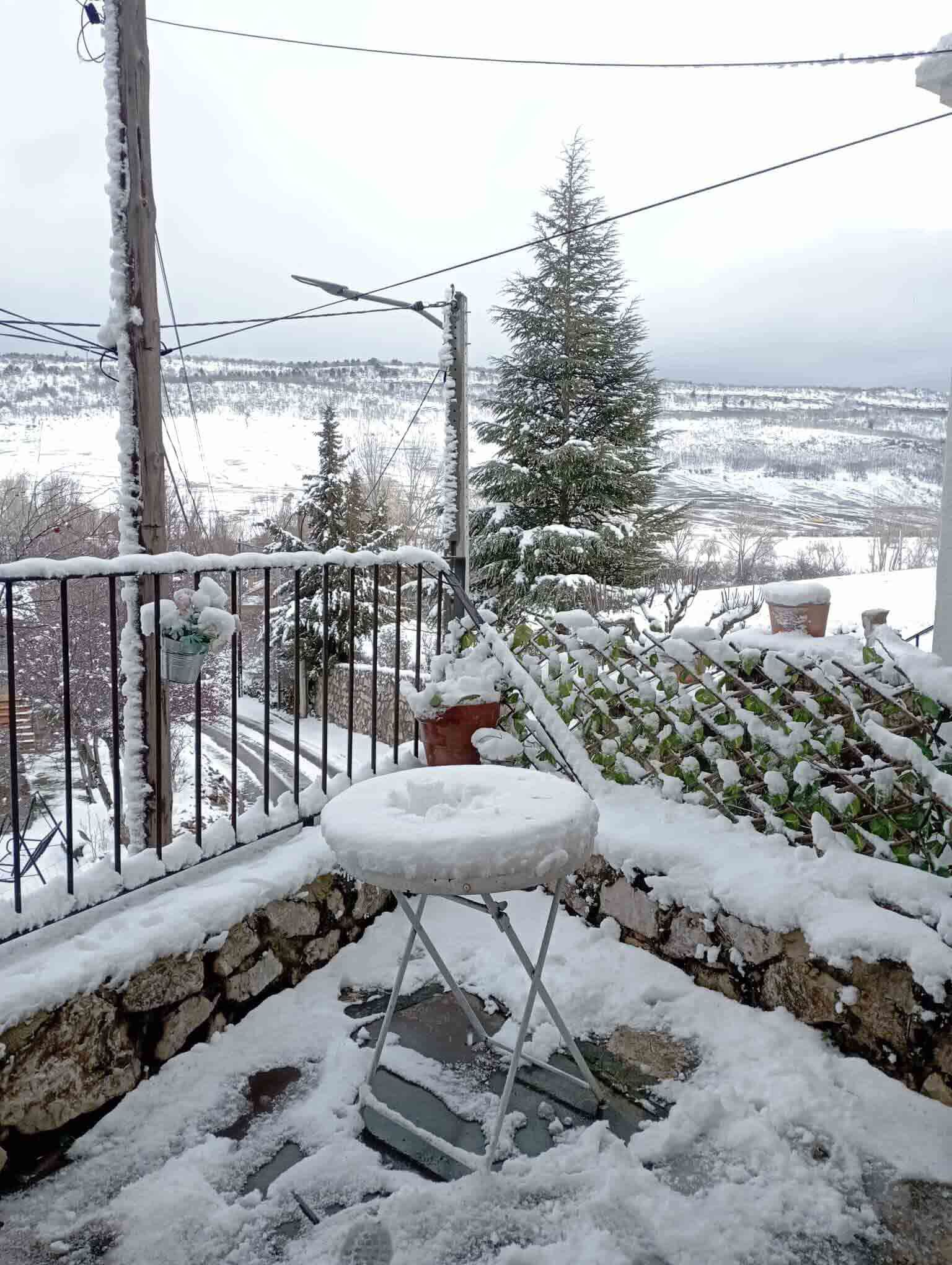 Una mesa y una silla están cubiertas de nieve en un balcón.