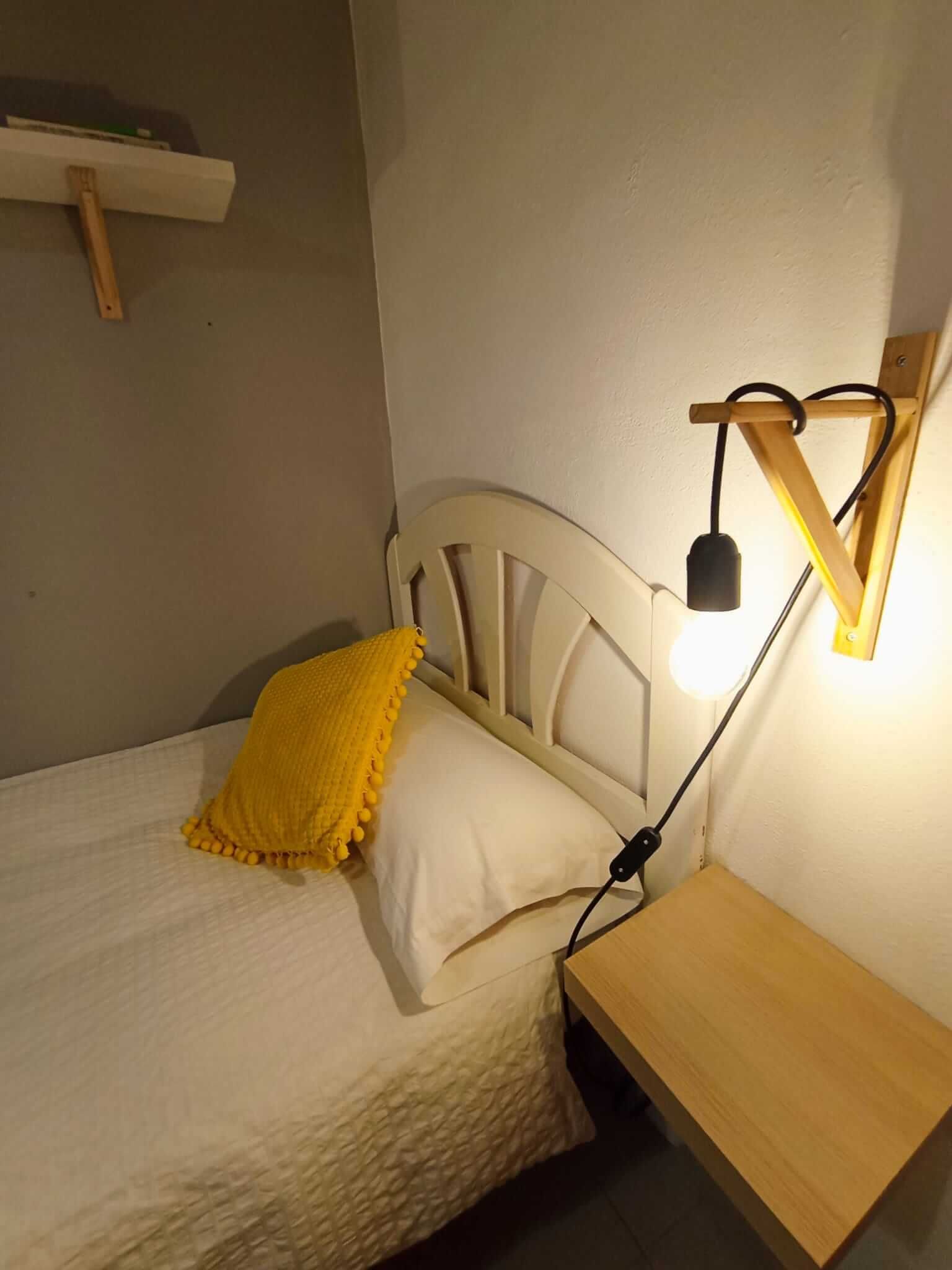 Un dormitorio con una cama, mesita de noche, lámpara y un estante.